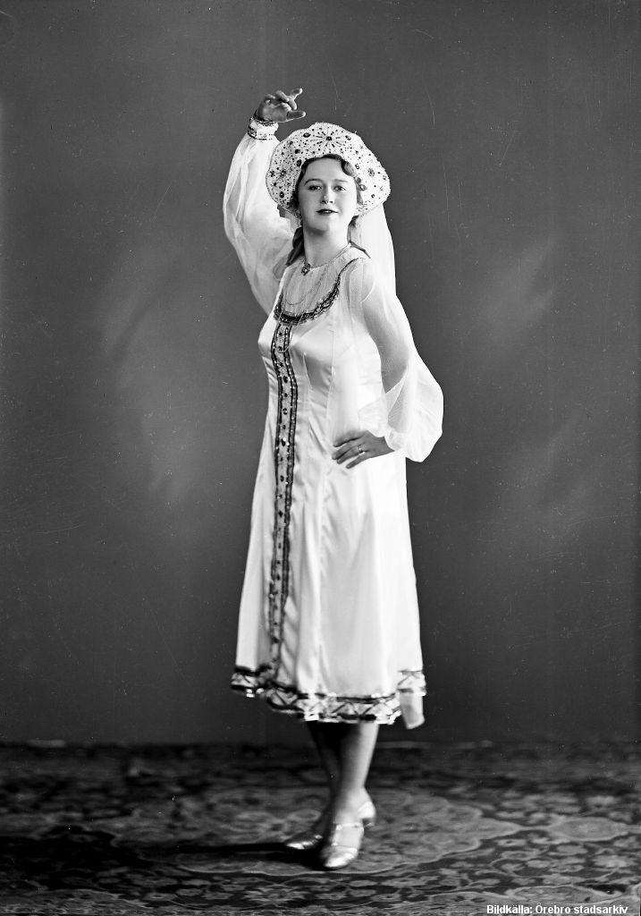 En kvinna i vita kläder poserar dansant.