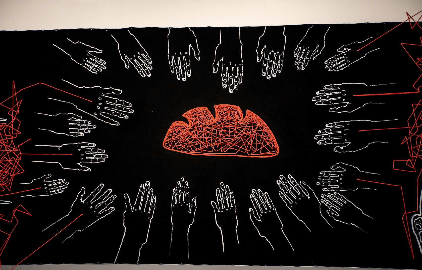 Black canvas stretching over 20 meters with white paintings and red lines. Lots of hands reaching for a loaf of bread.