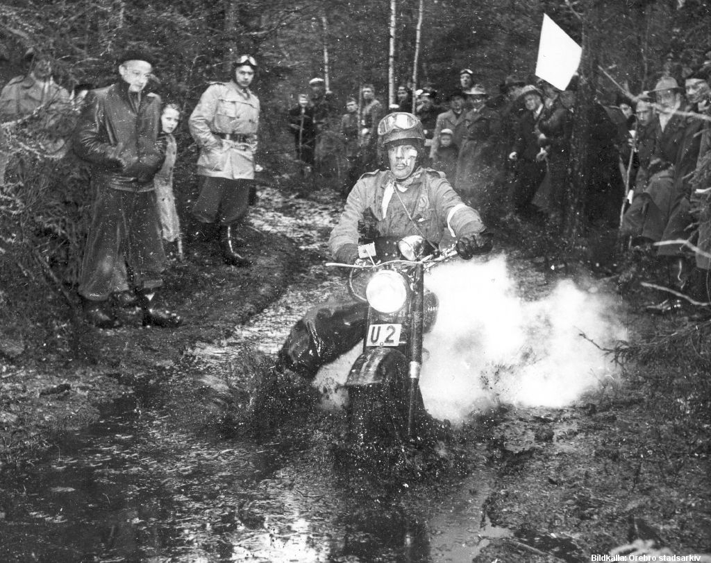 En man åker motorcykel i lervälling. Publik står på båda sidor om lerbanan.