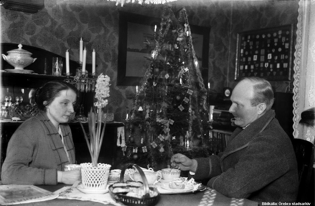 Kvinna och man vid dukat kaffebord. I bakgrunden en julgran.
