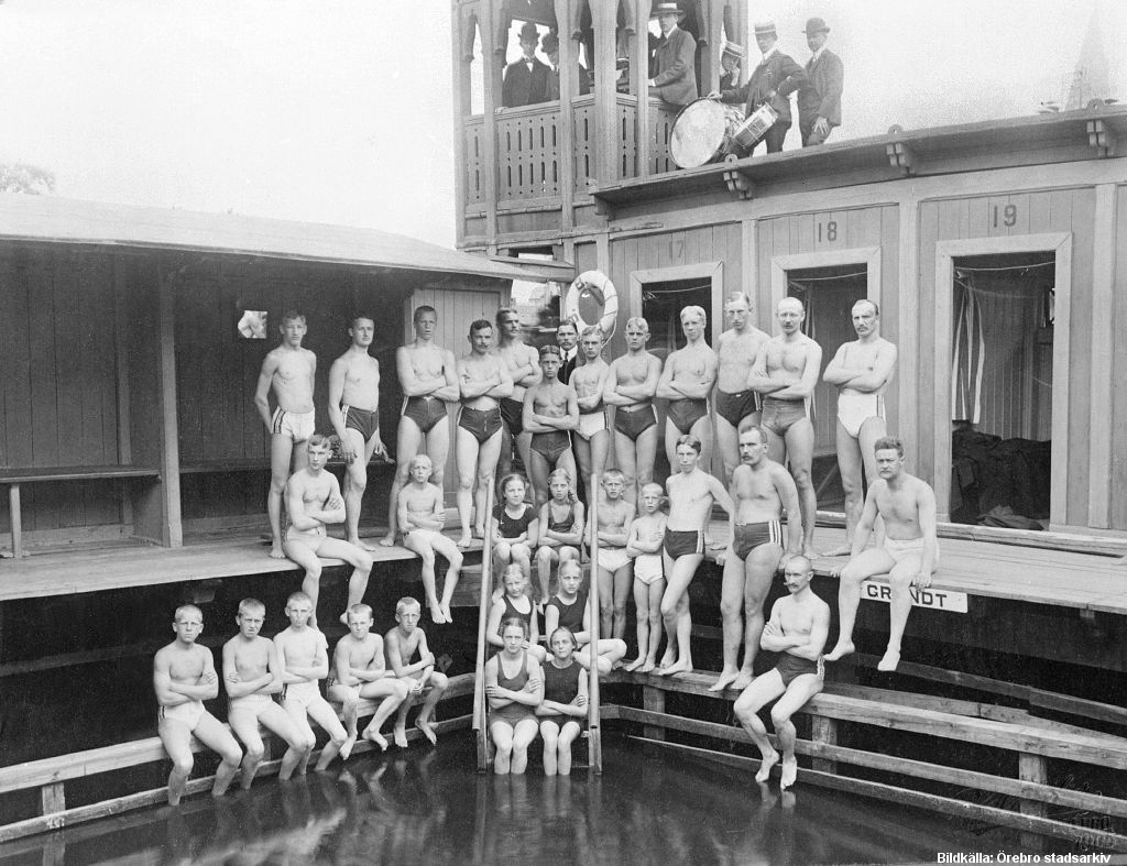 Gruppbild med badklädda barn och vuxna män som står vid en bassängkant.