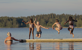 barn hoppar i vattnet från brygga i sjö i kvällsljus