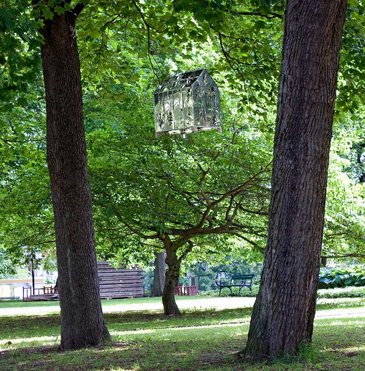 Uppe i luften mellan två träd hänger ett litet silvrigt växthus. 