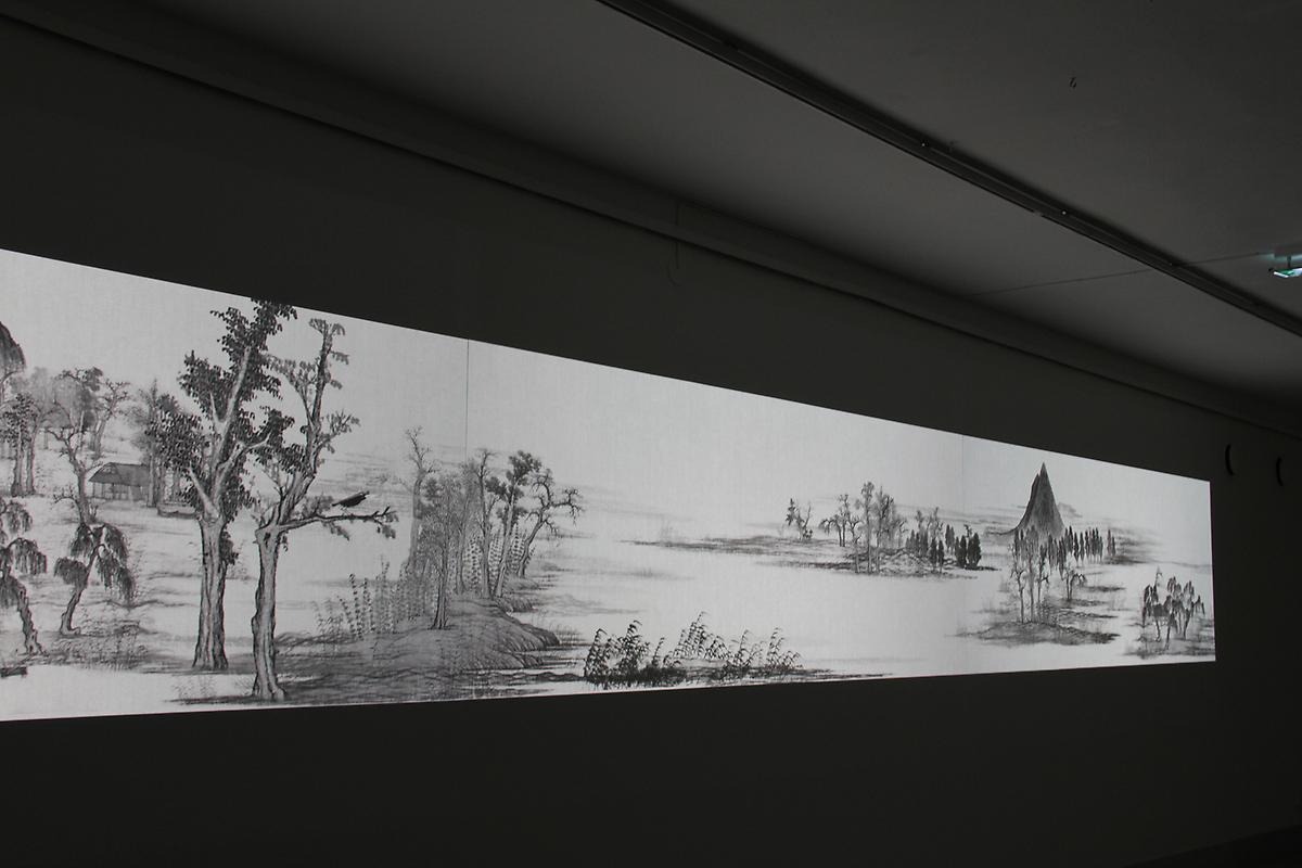 I ett mörkt rum sträcker sig en avlång animation av en tecknad målningar i svart vitt. Teckningen föreställer ett landskap med olika växtligheter. 