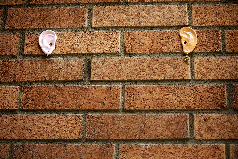 Två öron i keramik med örhängen är monterade på en tegelvägg.