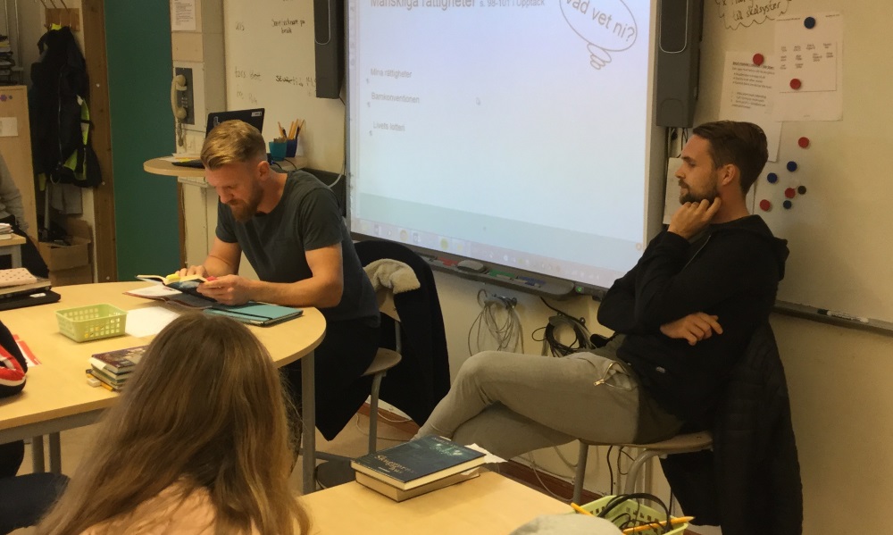 Två fotbollsspelare läser en bok framför elever