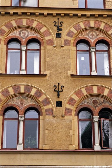 Detaljbild på husfasad. Gulmålad vägg med ornameterade fönster.